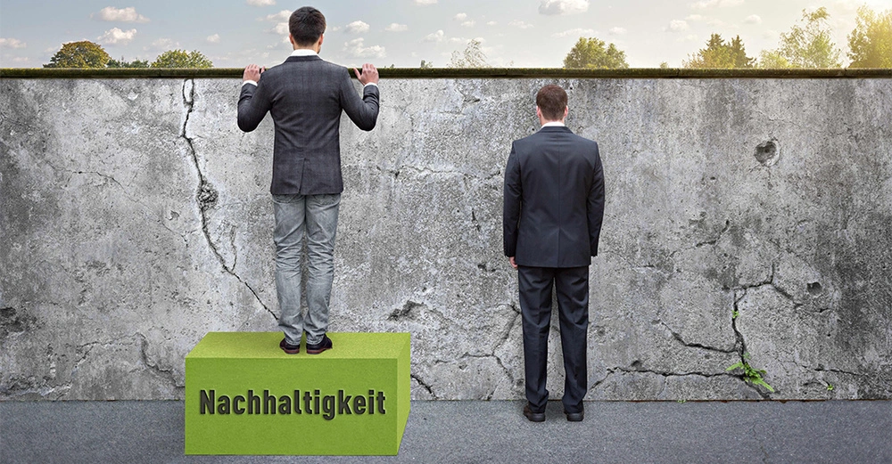 Mann steht auf grünem Block mit dem Text Nachhaltigkeit und blickt über eine graue Mauer während ein anderer Mann daneben auf dem Boden steht und die Mauer betrachtet im Freien mit Bäumen im Hintergrund