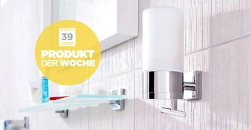 Seifenspender an der Wand in einem Badezimmer mit hellen Fliesen montiert Text 39 Produkt der Woche Blurry Regale und Pflegeprodukte im Hintergrund