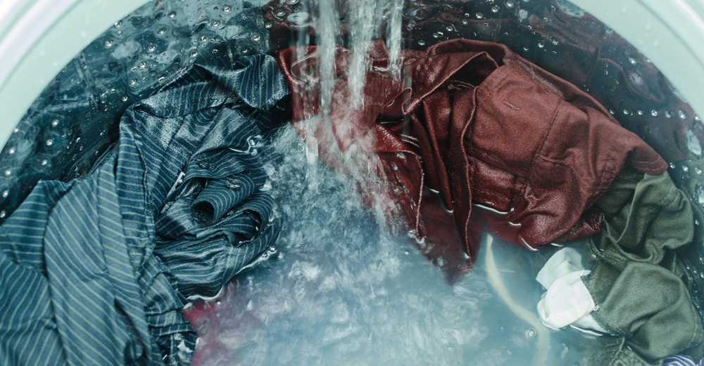 Kleidung rotiert im Inneren einer Waschmaschine Wasser fließt ein und vermischt sich mit den Kleidungsstücken die unterschiedliche Farben haben in einer metallischen Trommel