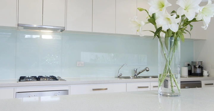 Ein hoher Glasvase mit weißen Blumen steht auf einer Küchenarbeitsplatte Vor einem Herd und einer Spüle in einer modernen weißen Küche