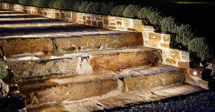 Steintreppen mit Beleuchtung führen in einem Garten hinauf umgeben von niedrigem Grün.