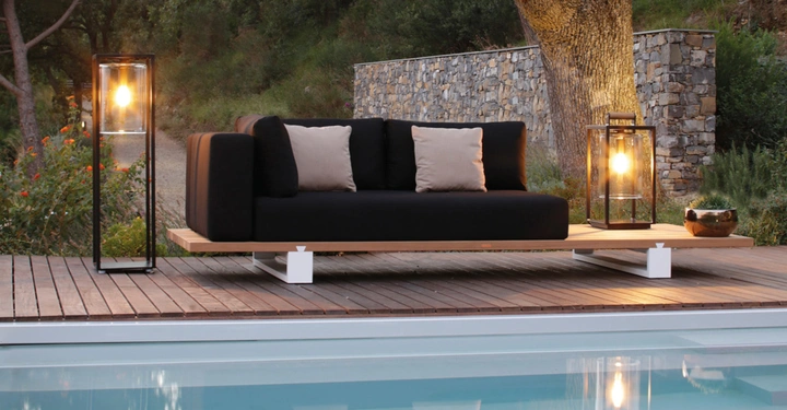 Schwarzes Sofa steht still auf einer Holzterrasse neben einem Pool umgeben von moderner Beleuchtung und Grünflächen im Freien