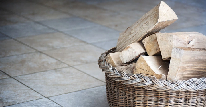 Ein Korb voller Holzscheite steht auf einem hell gefliesten Boden in einem Innenraum.