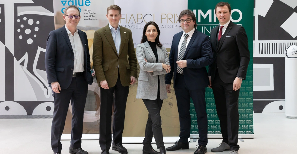 Fünf Personen posieren vor Werbebannern in einem modernen Innenraum. Texte auf Bannern: value one Länge mal Breite mal Höhe mal Freude FIABCI Prix d'Excellence Austria IMMY Innungspreis.