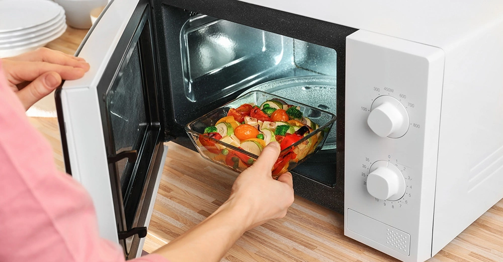 Eine Frau gibt eine Glasschüssel mit Gemüse in die Mikrowelle.