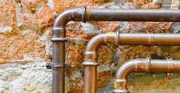 Kupferrohre verlaufen an einer alten Backsteinmauer entlang.