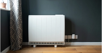 Moderner Elektroheizkörper steht für dunkelgrüner Wand und Eichenparkett. Links ein passender Vorhang.