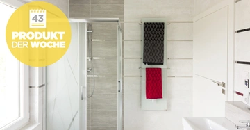 Duschkabine steht in einem modernen Badezimmer mit grauen Fliesen. An der Wand hängen zwei Handtücher. Links erscheint ein gelber Button mit der Aufschrift 43 PRODUKT DER WOCHE.