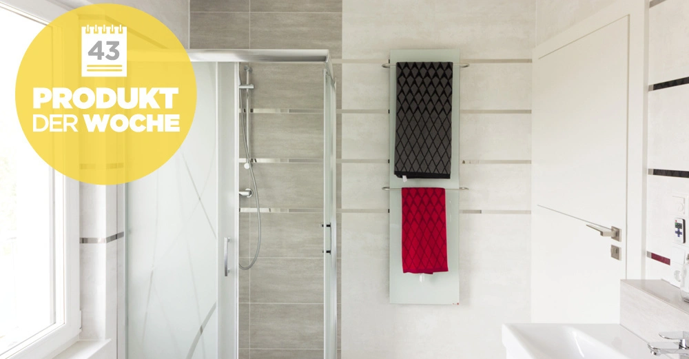 Duschkabine steht in einem modernen Badezimmer mit grauen Fliesen. An der Wand hängen zwei Handtücher. Links erscheint ein gelber Button mit der Aufschrift 43 PRODUKT DER WOCHE.