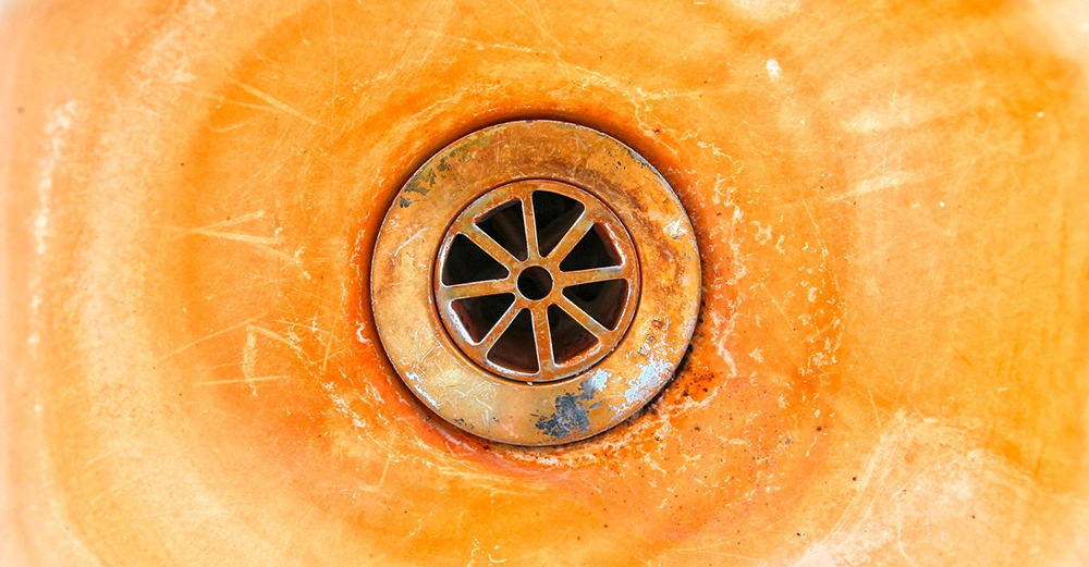 Ein rostiger Abfluss in der Mitte eines orangefarbenen, fleckigen Waschbeckens