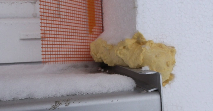 Galerie-Bild 15: Schneebedecktes Fensterbrett aus Metall Fixiermasse um Fensterabschluss herum Befindet sich außen an einer weiß verputzten Wand daneben orangefarbenes Baugewebe