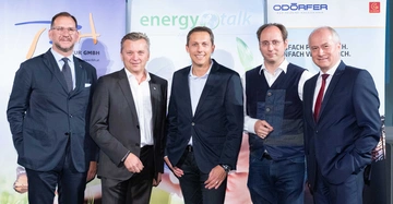 Fünf Männer tragen Anzüge und posieren nebeneinander. Sie stehen vor Bannern mit der Aufschrift tbh.at, energy.talk und ODÖRFER BAD HEIZUNG HAUSTECHNIK.