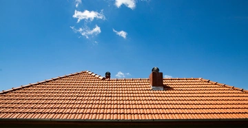 rotes Ziegeldach mit 2 Kaminen vor strahlend blauem Himmel mit kleinen Wölkchen