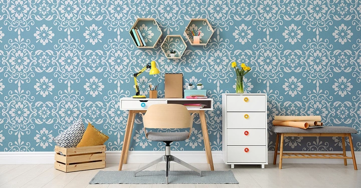 Hellblaue Tapete mit großen floralen Mustern. Im Vordergrund kleiner Beistelltisch und Sideboard sowie weiße Kommode mit 4 Schubladen. An der Wand hängen zwei runde Bilder.