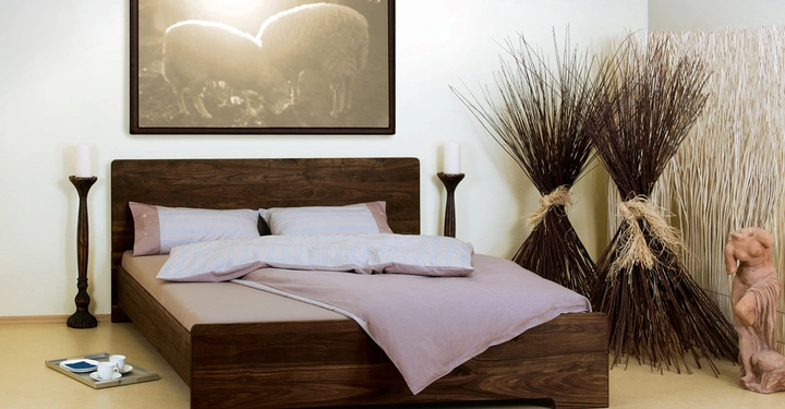 Galerie-Bild 2: Holzbett ist mit lila Bettwäsche bezogen zwei lila Kissen darauf Im Hintergrund hängen zwei Büschel trockener Zweige und eine Statue Tiere Gemälde über dem Bett Nachtisch mit Tassen rechts