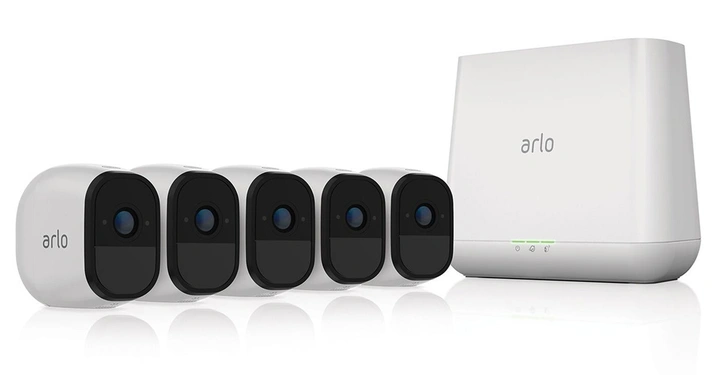 Fünf kleine weiße Kameras mit schwarzen Fronten und blauen Linsen stehen nebeneinander vor einer größeren weißen Basisstation mit der Aufschrift arlo.