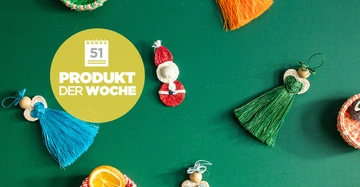 Gestrickte weihnachtliche Figuren liegen auf grünem Hintergrund. Ein gelber Kreis in der linken Mitte enthält Text: "51 PRODUKT DER WOCHE".