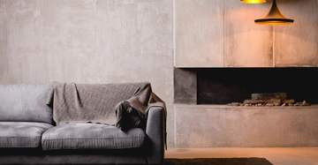 Cleanes, modernes Wohnzimmer mit grauer Couch und brauner Decke vor Wand aus Sichtbeton und betoniertem offenem Kamin