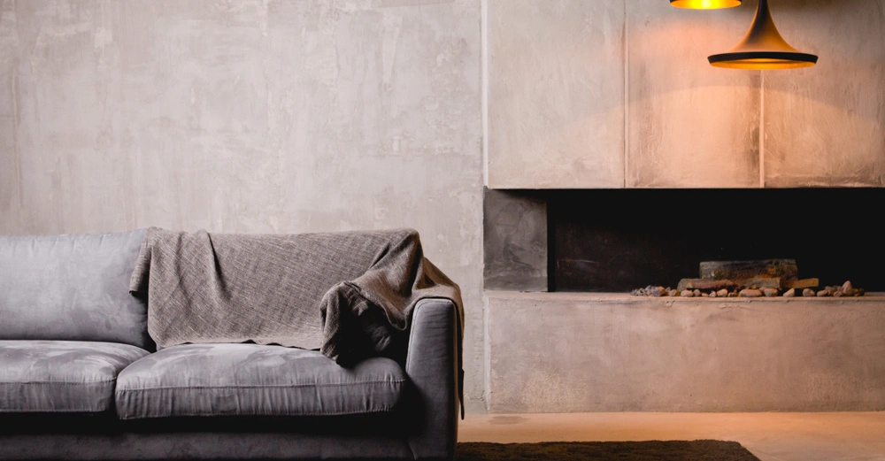 Cleanes, modernes Wohnzimmer mit grauer Couch und brauner Decke vor Wand aus Sichtbeton und betoniertem offenem Kamin