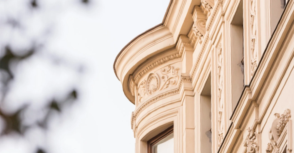 Ein detailliertes Gebäude zeigt reich verzierte Fassaden und Fensterrahmen darunter unscharfe Bäume im Vordergrund.