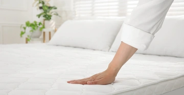 Frau mit weißer Bluse streicht mit Hand über weiße Matratze