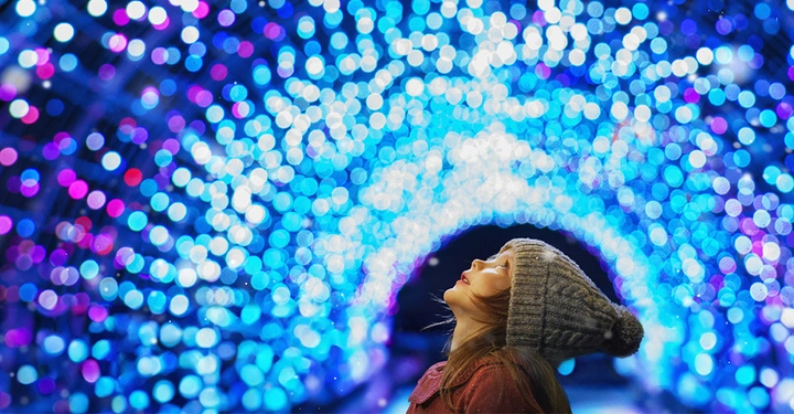 Kind mit Wintermütze staunt in einem magischen Tunnel aus blauer LED-Weihnachtsbeleuchtung.