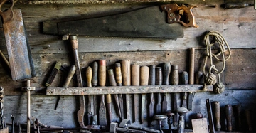 Werkzeuge hängen und stehen unbenutzt in einem Holzregal an einer rustikalen Holzwand in einer Werkstatt.