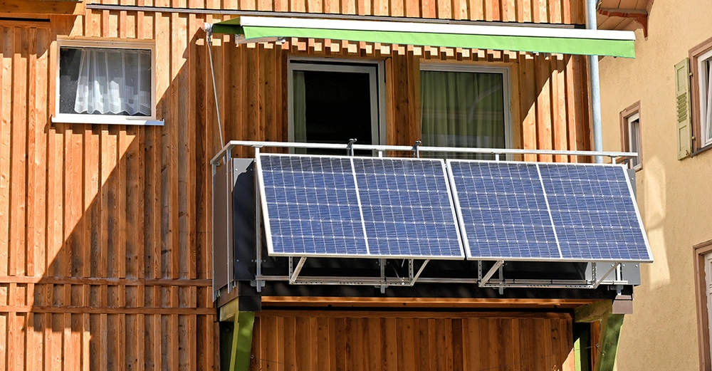 Auf dem Balkon eines Wohnhauses mit Holzfassade sind zwei Photovoltaik-Module montiert