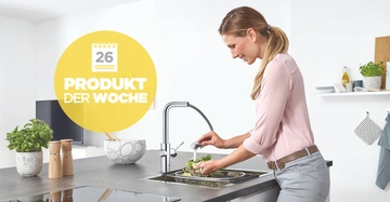 Eine Person wäscht Gemüse in einer modernen Küche unter einem Wasserhahn. Text auf gelbem Kreis: 26 PRODUKT DER WOCHE.