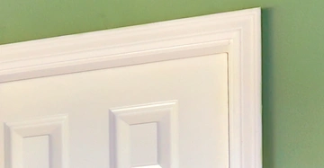 Oben rechts einer weißen Tür mit erhabenen rechteckigen Paneeldetails vor einer grünen Wand in einem Innenraum.