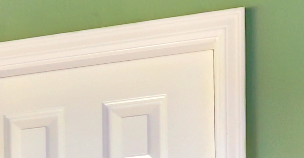 Oben rechts einer weißen Tür mit erhabenen rechteckigen Paneeldetails vor einer grünen Wand in einem Innenraum.