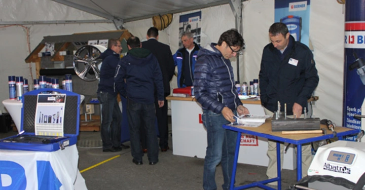 Galerie-Bild 5: Personen arbeiten und interagieren an verschiedenen Ständen in einem Zelt. Sie begutachten Produkte auf Tischen mit Maschinen und Materialien. Im Hintergrund sind weitere Stände und Regale sichtbar.