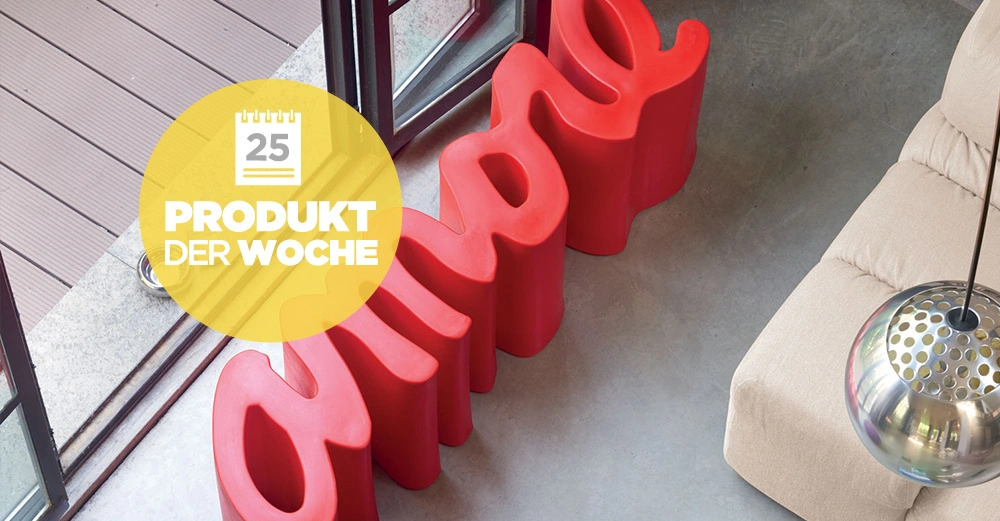 knallrote AMORE Sitzbank liegt in einem Wohnzimmer vor der Terrassentür. Im Hintergrund ein beiges Sofa angeschnitten.