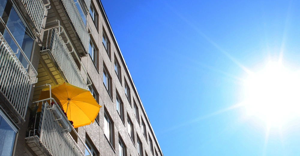 Gelber Sonnenschirm auf einem Balkon eines mehrstöckigen Wohngebäudes im Sonnenlicht eines klaren blauen Himmels.