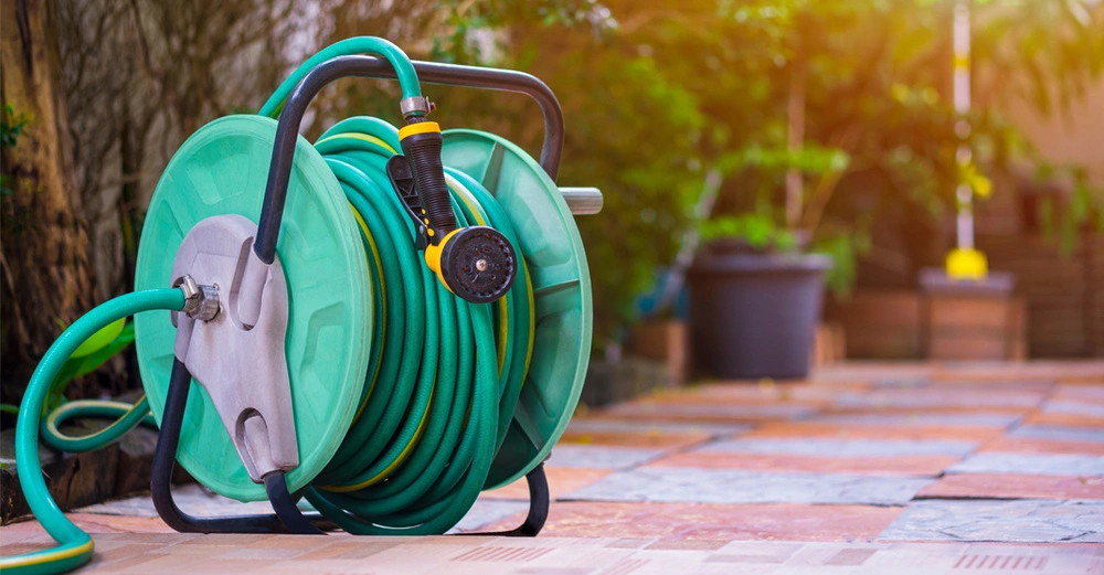 Schlauchtrommel mit aufgerolltem grünen Gartenschlauch steht auf der Terrasse.