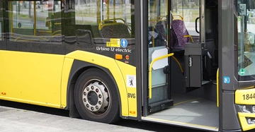 Gelber Stadtbus steht an einer Haltestelle die Tür ist geöffnet Sitzplätze im Inneren sind sichtbar Schriftzug Urbino 12 electric und BVG-Logo an der Seite städtischer Hintergrund