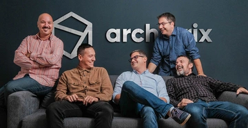 Fünf Männer sitzen auf einem grauen Sofa und lächeln und unterhalten sich fröhlich. Im Hintergrund ist eine dunkle Wand mit dem Text "archviz" und einem geometrischen Symbol.