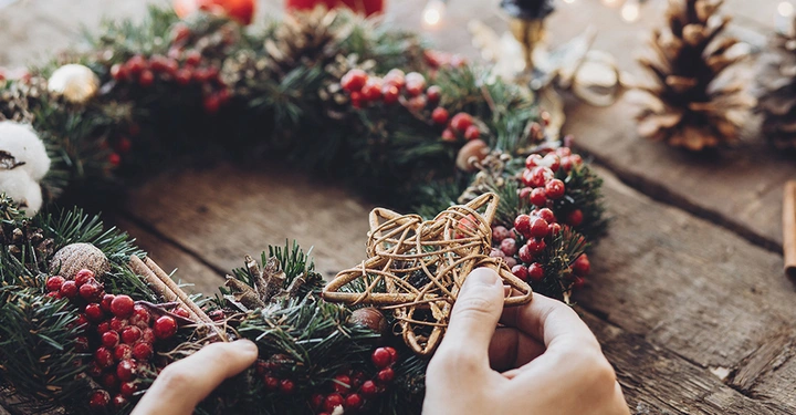 Dekorieren eines Adventskranzes mit Stern und Zapfen: Der runde Kranz symbolisiert im christlichen Glauben die Ewigkeit und Gottes Liebe.