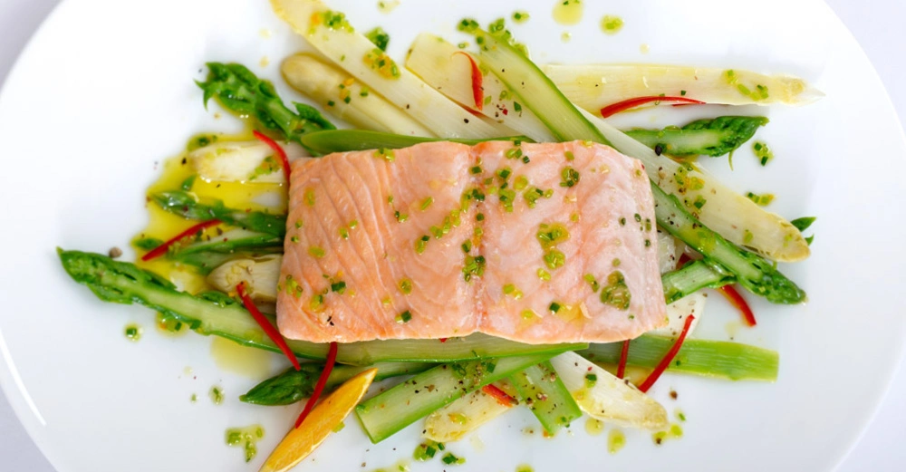 Frischer gedünsteter Lachs auf einem Bett aus dampfgegartem Gemüse. Sehr appetitlich auf Teller angerichtet. 