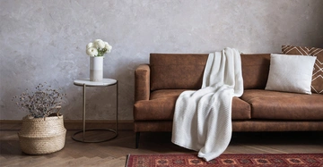 Braunes Sofa mit weißer Strickdecke und weißem Beistelltisch.