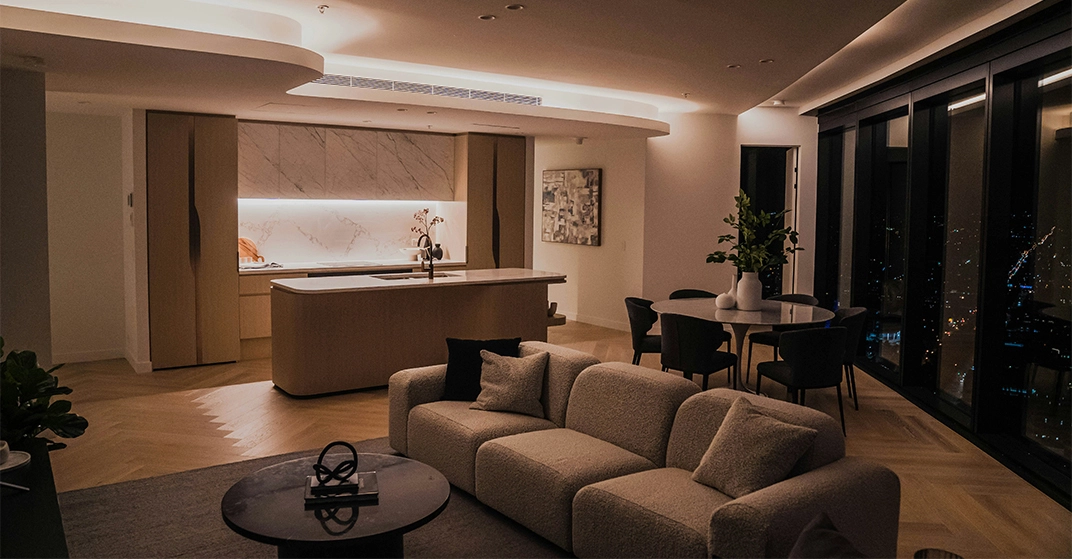 Eleganter, offen gestalteter Wohn- und Essbereich mit moderner Kücheninsel, gemütlichem Sofa, großflächigen Fenstern und stimmungsvoller indirekter Beleuchtung in einer hochwertigen Stadtwohnung bei Nacht.