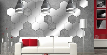 Weiße Couch mit roten Kissen steht vor einer Wand aus silbernen sechseckigen Spiegeln. Im Raum befinden sich graue Deckenlampen, eine Stehlampe und Wanddekoration in einem modernen Wohnraum.