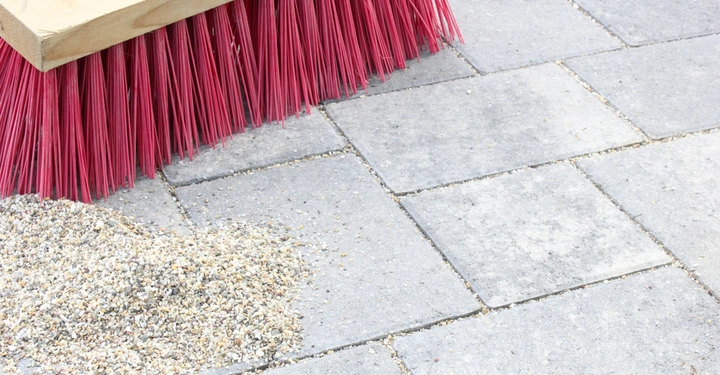 Roter Besen fegt Kieselsteine auf grauem Pflastersteinen im Freien