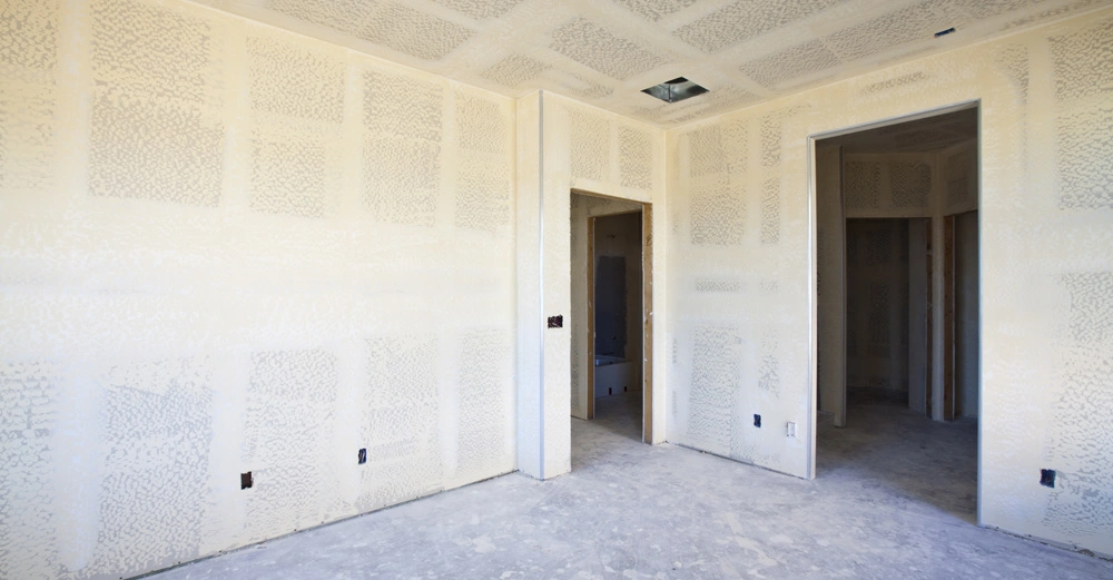 Raum ohne Möbel Bauphase zeigt frisch verputzte Wände mit Spachtelmaserungen offener grauer Betonboden zwei Türen führen zu angrenzenden Räumen leichtes Baustellenchaos.