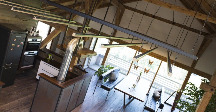 Galerie-Bild 2: Küche mit schwarzem Kühlschrank und Beistelltisch, umgeben von Holzbalken. Neben der Küche ein Essbereich mit Holzbank, großem Tisch und Schmetterlingsdekorationen vor einem großen Fenster.