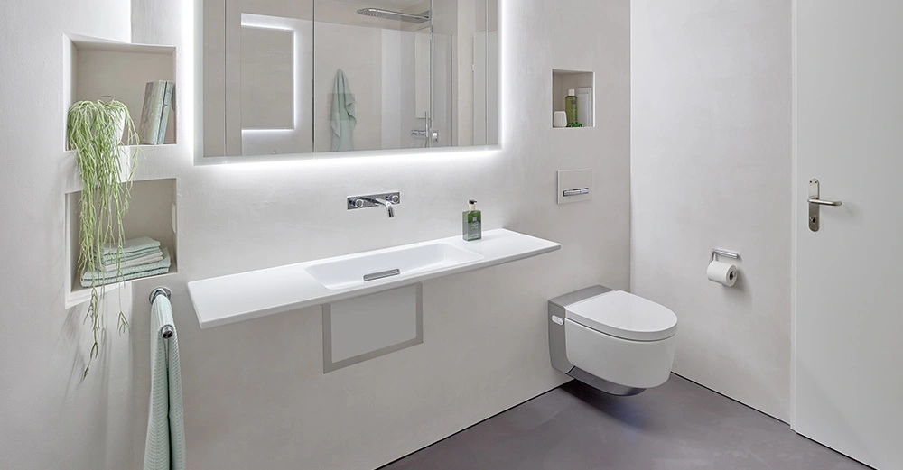 Ein weißes Badezimmer mit schwebendem Waschbecken und wandhängender Toilette in einer modernen, minimalistischen Umgebung. Handtuchhalter, Regale mit Pflanzen und Pflegeprodukten links und rechts vorhanden.