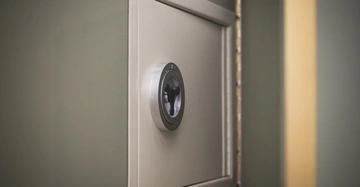 Ein kleiner Tresor mit Drehknopf ist an einer grünen Wand montiert. Der Tresor ist leicht geöffnet, wobei das Scharnier und ein Teil des Inneren sichtbar sind.