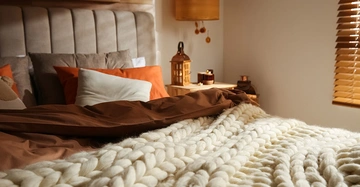 Eine große weiße Wolldecke liegt auf einem Bett in einem herbstlich gehaltenen Schlafzimmer.