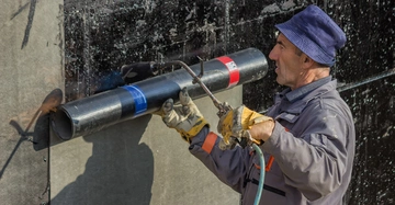 Arbeiter verlegt konzentriert schwarze Bitumenbahnen auf der Innenseite eines Kellers.