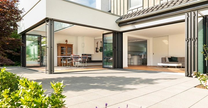 Galerie-Bild 2: Große Glasschiebetüren verbindet den modernen Innenraum eines Hauses mit einem geräumigen Terrassenbereich Der Innenraum beinhaltet einen Holztisch mit Stühlen ein Sofa und eine Küche